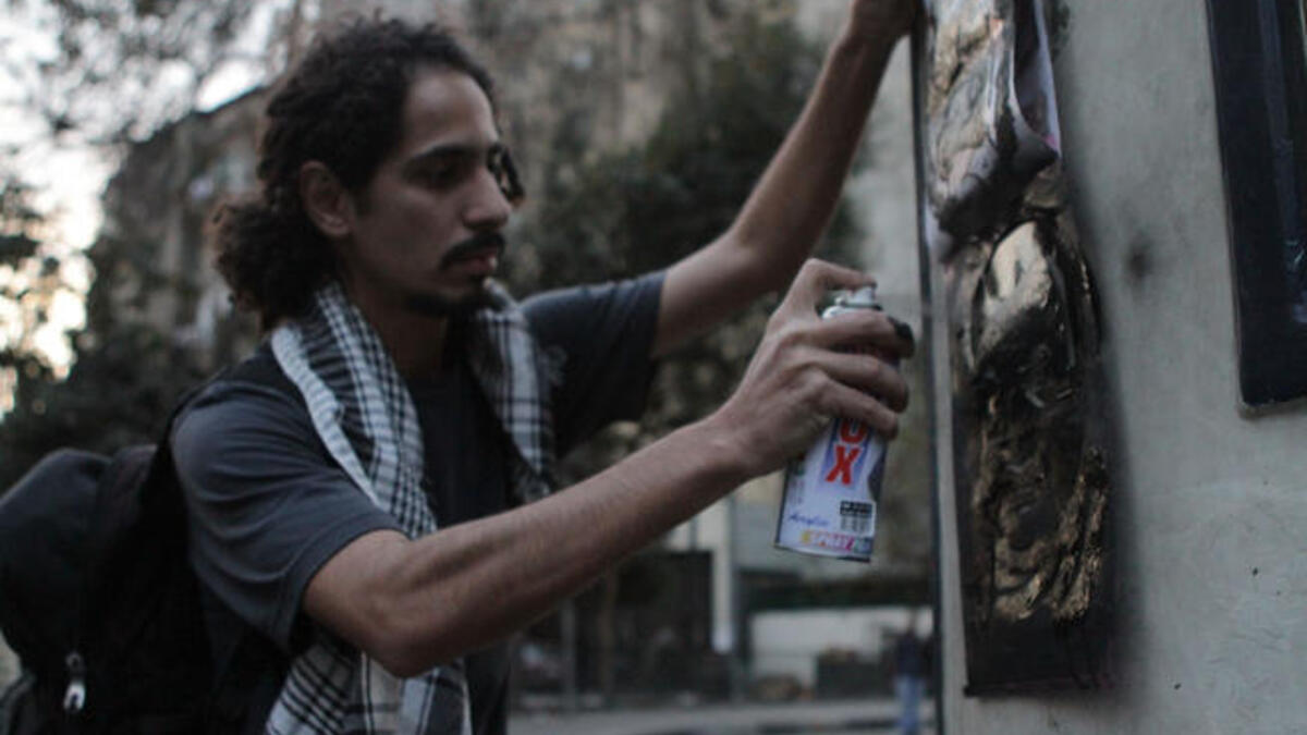 An Egyptian man spraying a graffiti paint on the the wall.