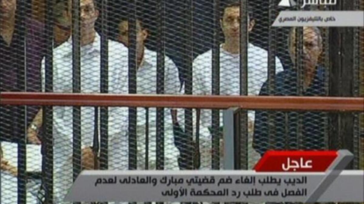 Egyptian former interior minister Habib al-Adly (R) stands along side Alaa (2nd R) and Gamal (L) Mubarak in a cage-like holding cell in the court room in the police academy.