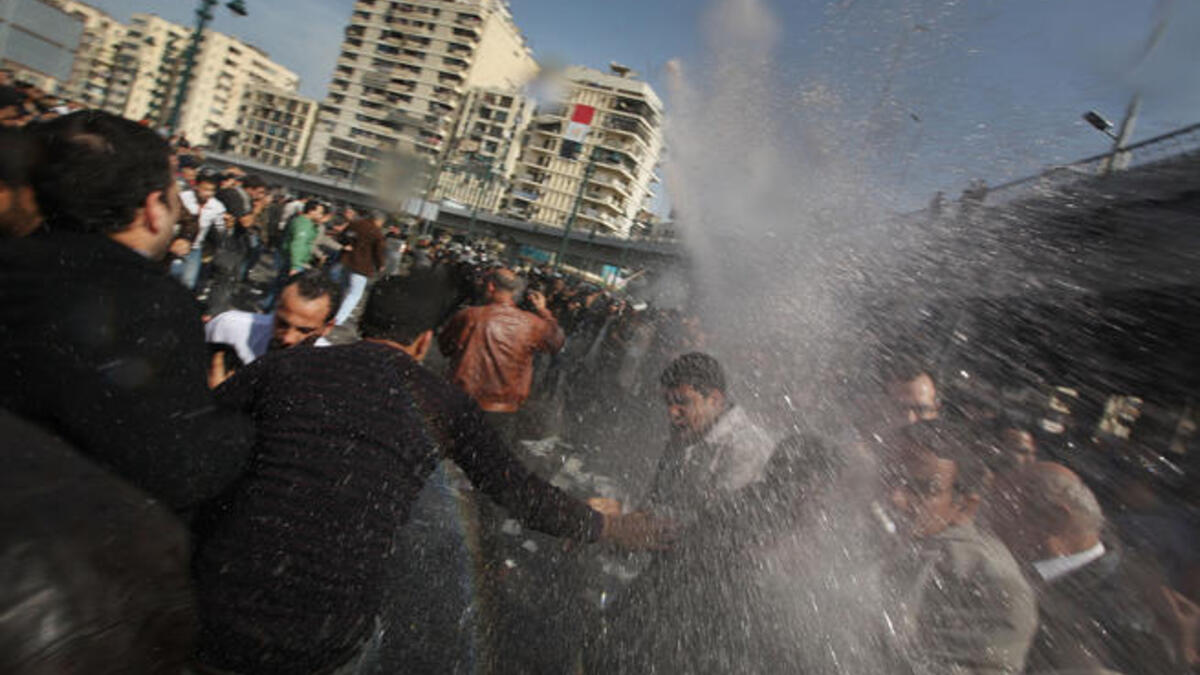 Protesters are hit by a water cannon in front of The l-Istiqama Mosque, as they're watched by riot police in Giza.