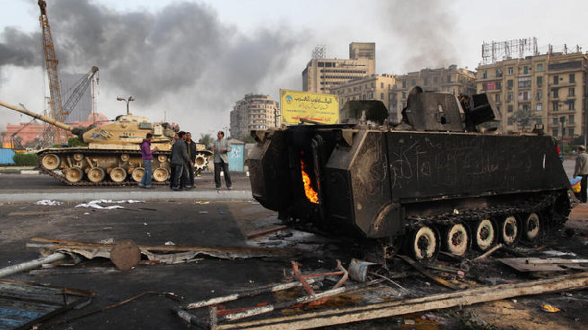 An army tank stands near the remains of a burnt out armored personnel carrier in Tahrir Square.