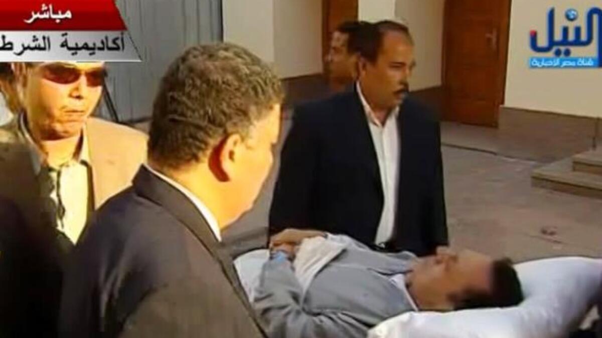 Another hearing, another pair of PJs: Still on a trolley- entering and leaving the docks' metal defendants' cage, flanked by his
two sons. On this second public trial appearance, August 15th, he tries for a smarter pajama- a
grey jacket , like a robe, or outer garment, over the white night shirt; adding a little panache to the hospital whites.