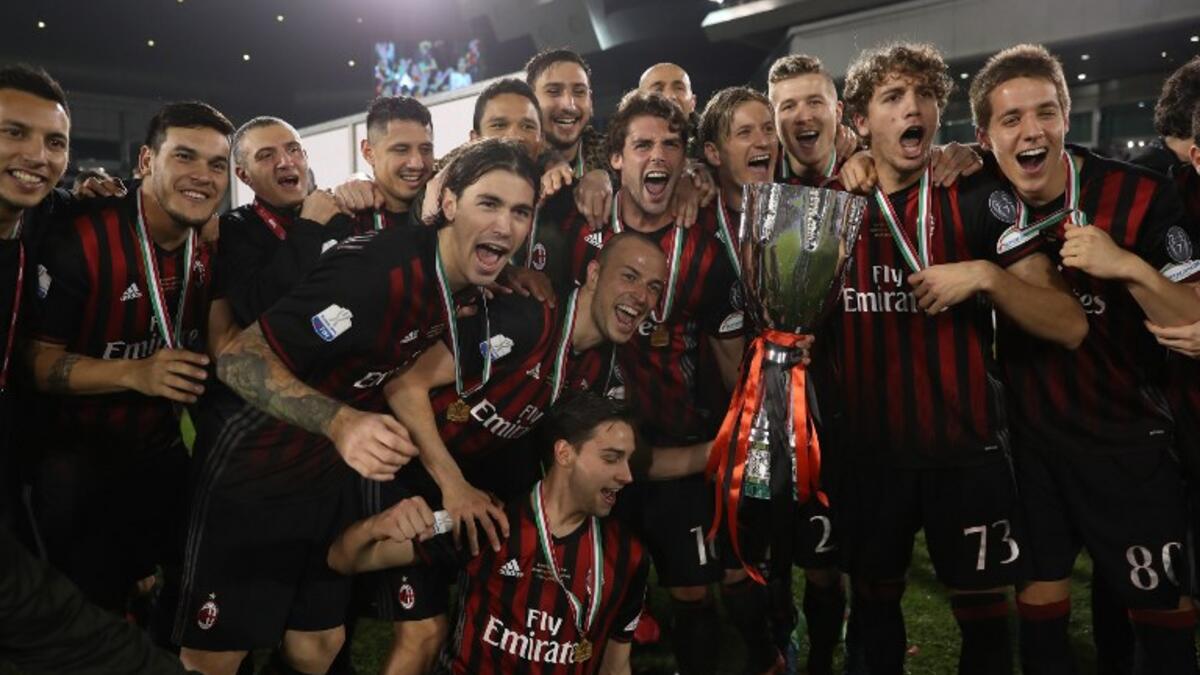 AC Milan's players pose with the trophy after winning against Juventus during the Italian Super Cup final match between AC Milan and Juventus in Doha on December 23, 2016. AC Milan beat Juventus to win the Italian Super Cup in a penalty shootout, the first trophy the Rossoneri have won since 2011. KARIM JAAFAR / AFP