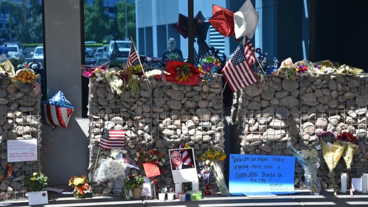 A passerby is reflected in glass as he collects himself before a makeshift memorial to Senator John McCain outside McCain's office in Phoenix, Arizona, August 27, 2018. McCain, a two-time US presidential candidate and war hero, passed away August 25 at the age of 81.  (Robyn Beck / AFP)