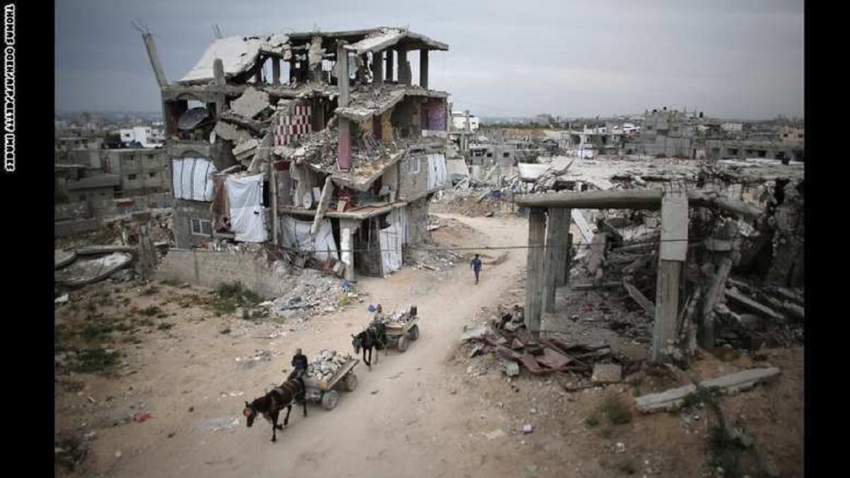 فلسطينيون يركبون عربات تجرها الحمير بين أنقاض مبان مدمرة في قطاع غزة، المباني تضررت بعد الحرب التي استمرت 50 يوماً بين إسرائيل وحماس عام 2014.