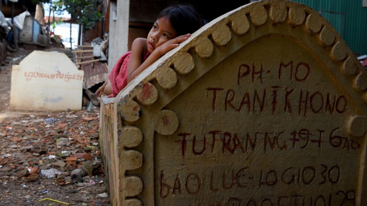 This picture shows a girl lying on a grave in Phnom Penh.  TANG CHHIN Sothy / AFP