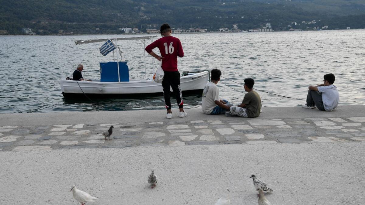 Migrant youth sit by a local fisherman at the city of Vathy on the island of Samos.  LOUISA GOULIAMAKI / AFP