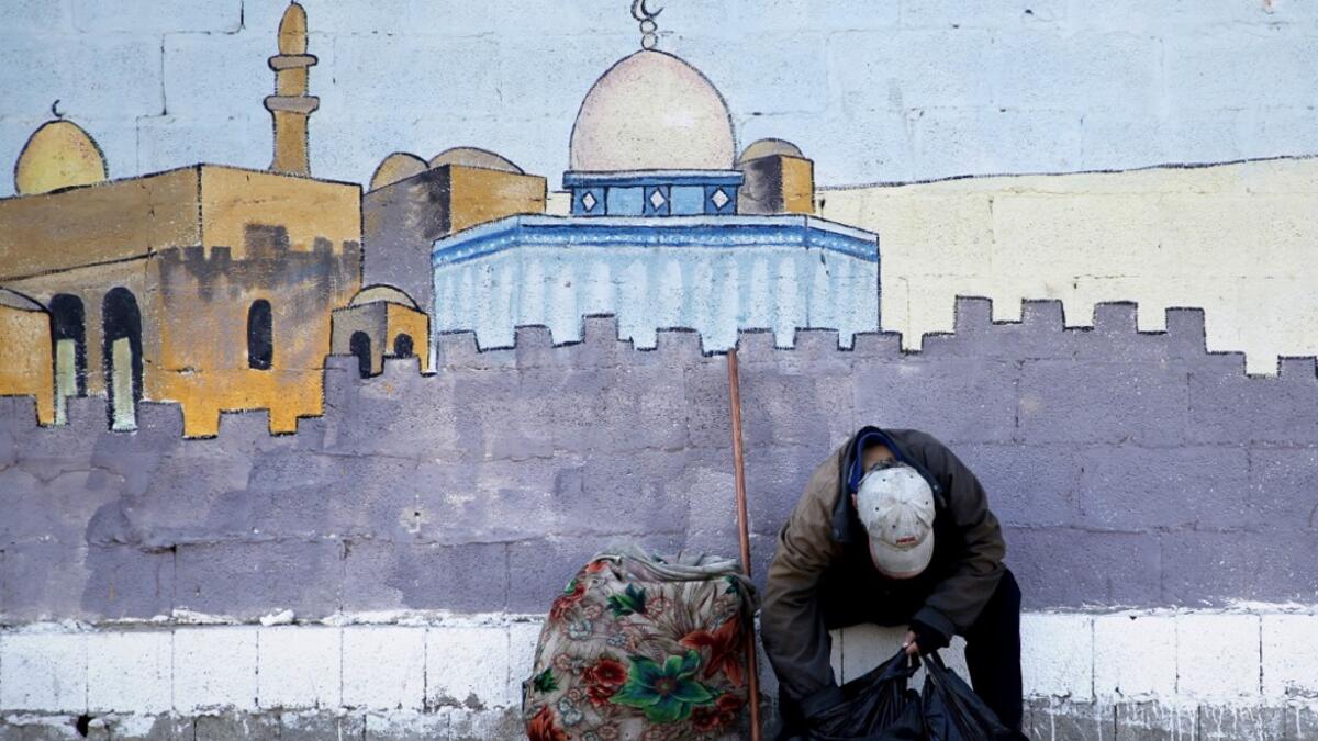 An impoverished Palestinian boy sits in front of a mural depicting the Dome of the Rock mosque in Jerusalem as he checks a bag containing things he collected from the streets in Gaza City on July 4, 2019.  MOHAMMED ABED / AFP