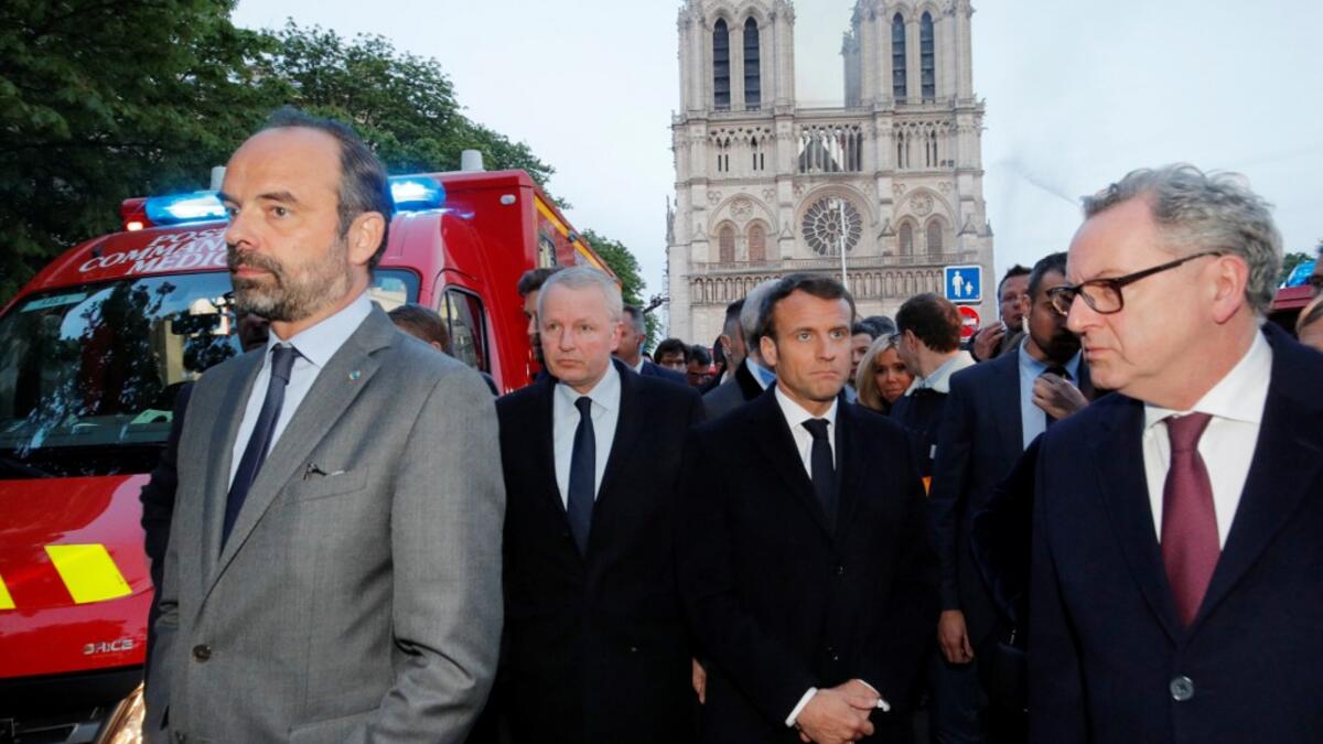 French Prime Minister Edouard Philippe (L), and French President Emmanuel Macron (3rd L) gather near the entrance of the Notre-Dame de Paris Cathedral in Paris, as flames engulf its roof on April 15, 2019. PHILIPPE WOJAZER / POOL / AFP