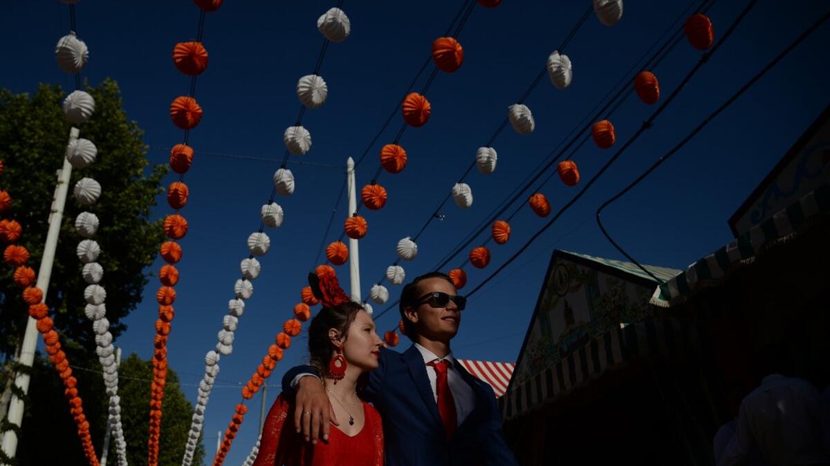 A couple walks past "casetas" (stalls) during the "Feria de Abril" (April Fair) festival in Seville on May 6, 2019. The fair dates back to 1847 when it was originally organized as a livestock fair but has turned into a week of flamenco dancing, music and bullfighting.  CRISTINA QUICLER / AFP