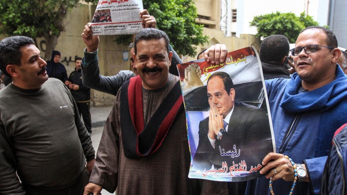 Egyptians pose for a picture with a newspaper front page and a poster of President Abdel Fattah al-Sisi outside a school in the second city of Alexandria during voting in a referendum on constitutional amendments on the first day of the three-day poll, on April 20, 2019. Tarek ABDEL HAMID / AFP